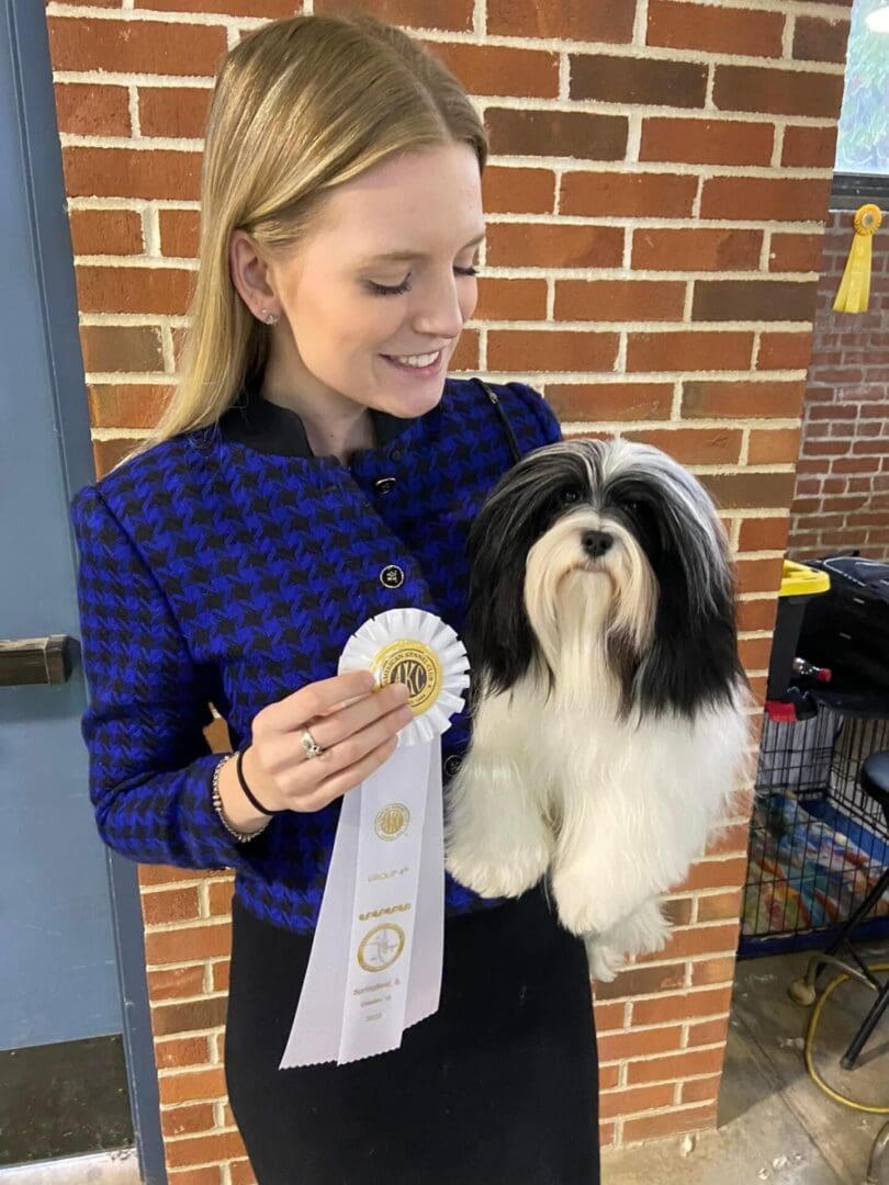 A woman holding a Havanese dog with a ribbon.