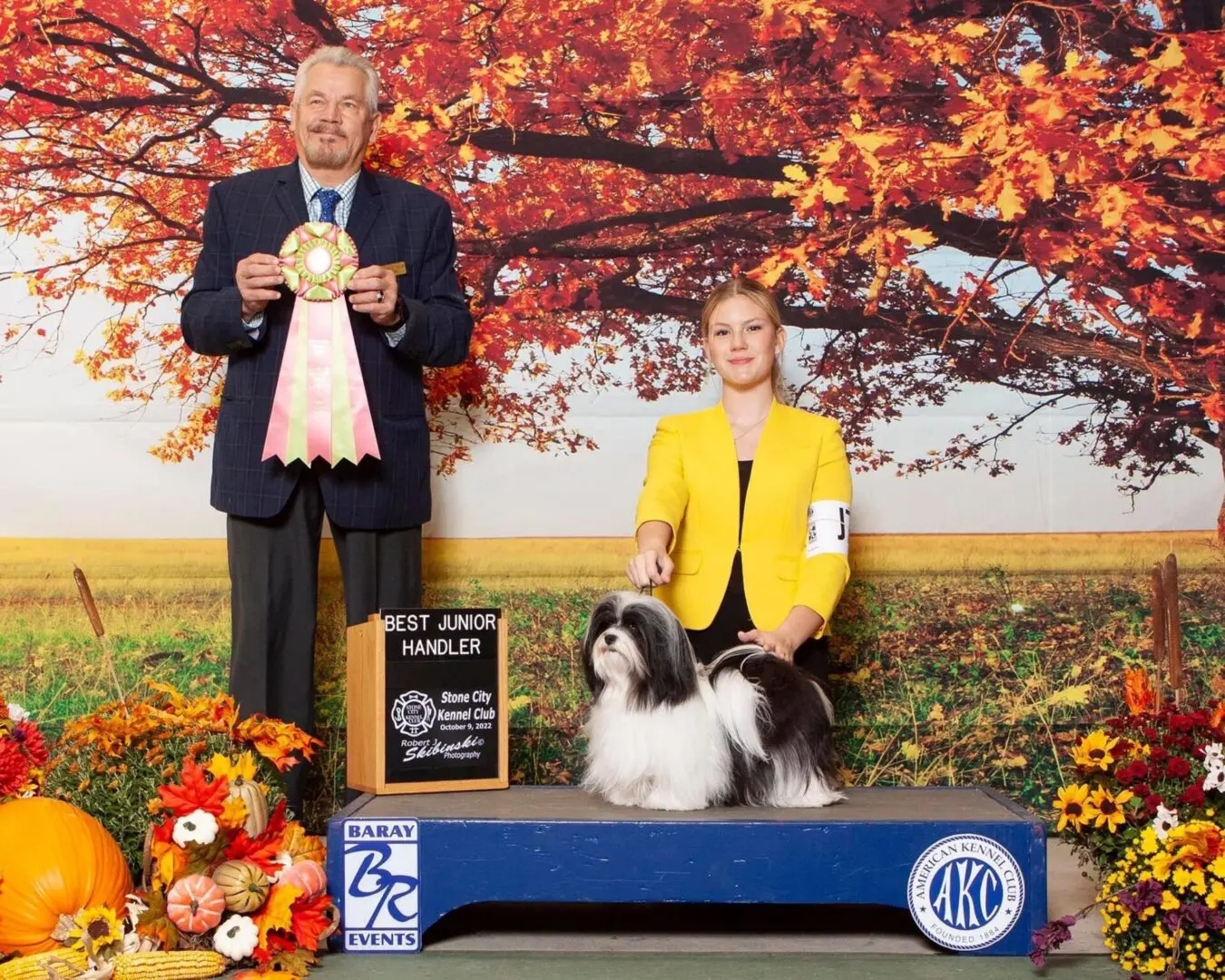 A man and woman standing next to a shih tzu puppy.