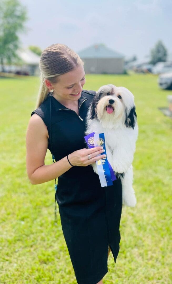 A woman in a black dress holding a white Havanese puppy.