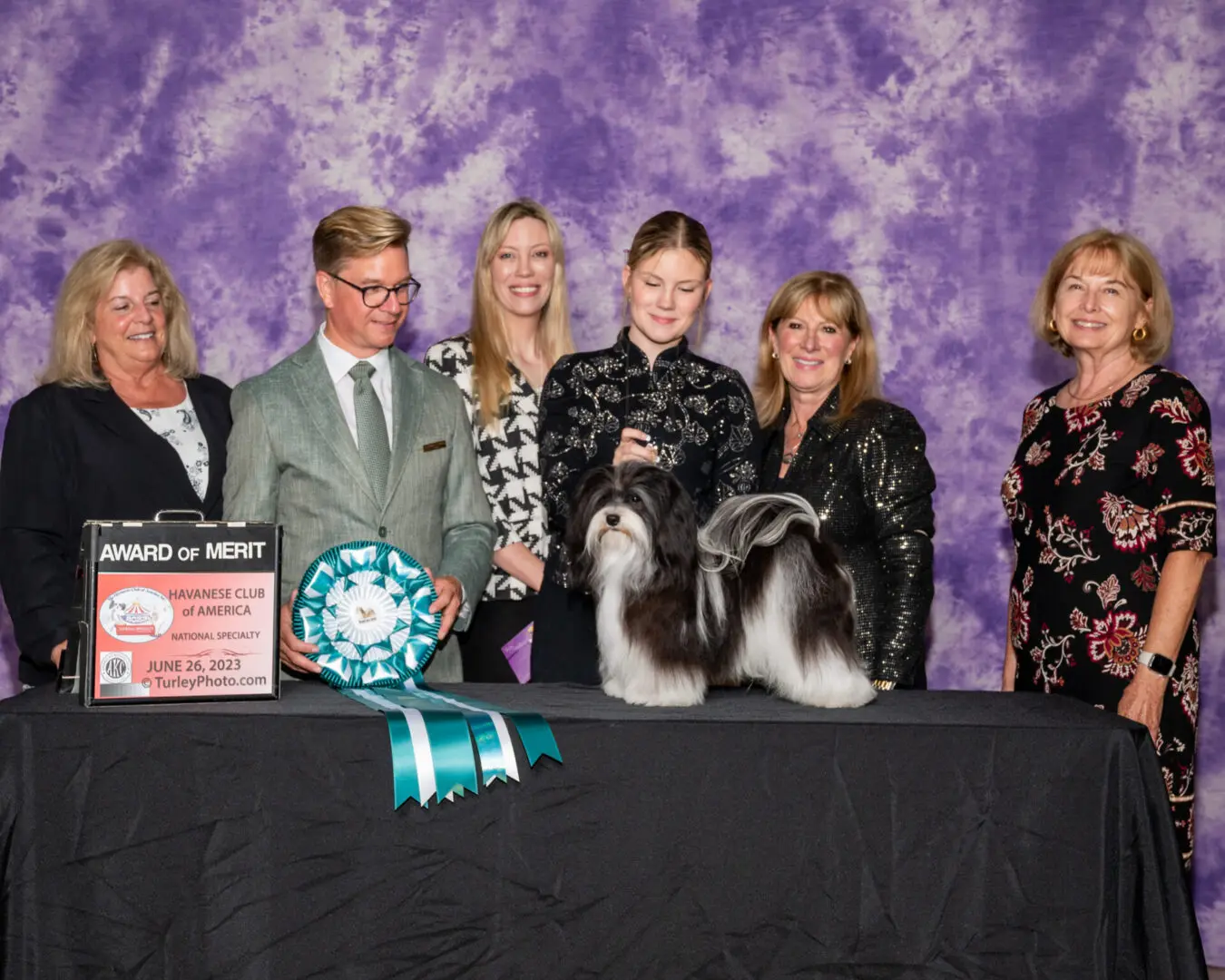 A group of people posing with a Havanese puppy.