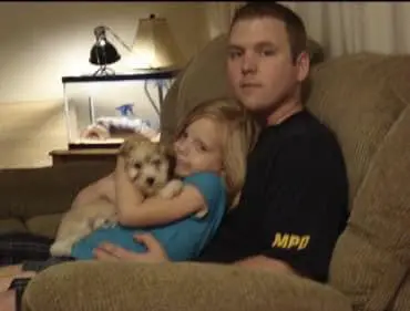 A man and a girl sitting on a couch holding a small Havanese puppy.