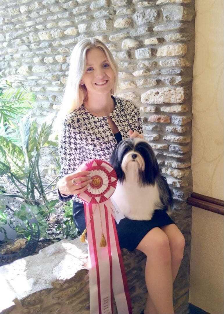 A woman poses with a shih tzu and a ribbon.